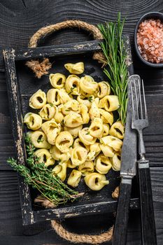 Italian traditional tortellini pasta with spinach in a wooden tray. Black wooden background. Top view.