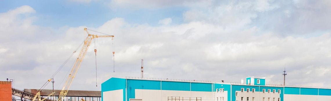 Machine crane at a construction site with a warehouse in an industrial area, panoramic view, high resolution.