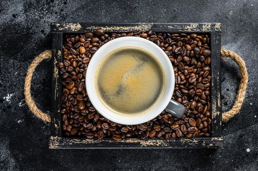 Coffee cup and beans in old wooden tray. Black background. Top view.