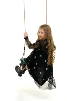 Beautiful little girl swinging in the studio on a swing. Concept of a happy childhood, family well-being.