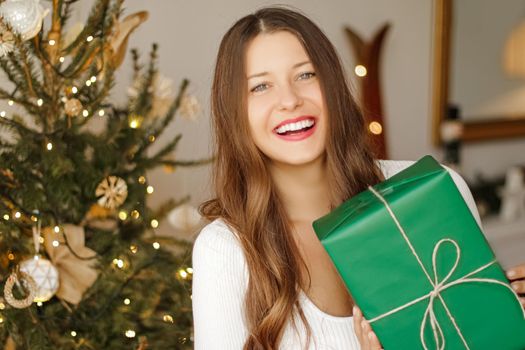 Christmas holiday and sustainable gifts concept. Happy smiling woman holding wrapped present with eco-friendly green wrapping paper.