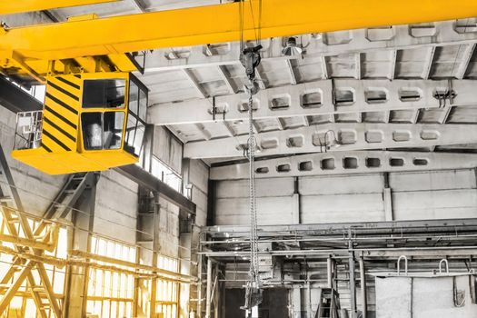 Overhead crane hoist equipment in an industrial plant transports an iron rail on lifting chain.