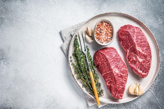 Raw Oyster Top Blade or flat iron roast beef meat steaks on a plate with herbs. White background. Top View. Copy space.