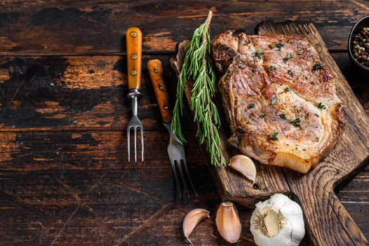 Roasted pork chop steak on a cutting board. Dark wooden background. Top view. Copy space.