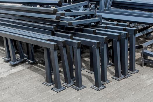 Pile of new metal structures or steel industrial material on paving slabs sidewalk at construction site.