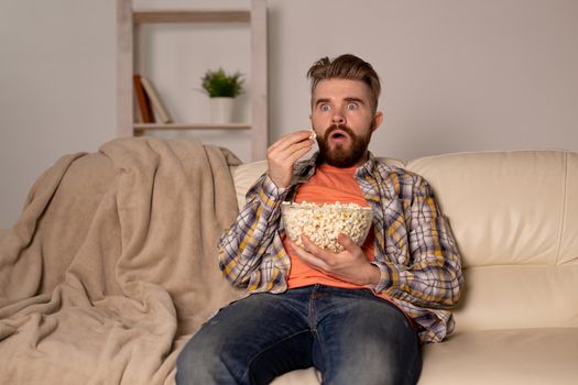 Bearded man watching film or sport games TV eating popcorn in house at night. Cinema, championship and fan.