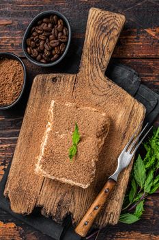 Italian dessert Tiramisu cake with cocoa and mint on a wooden board. Dark Wooden background. Top view.