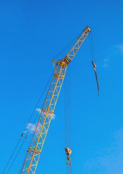 Hoisting machine industrial crane equipment against blue sky at construction site.