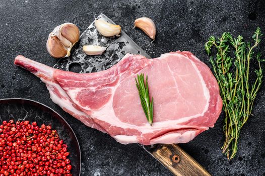 Raw tomahawk pork chop meat steak on a meat cleaver. Black background. Top view.