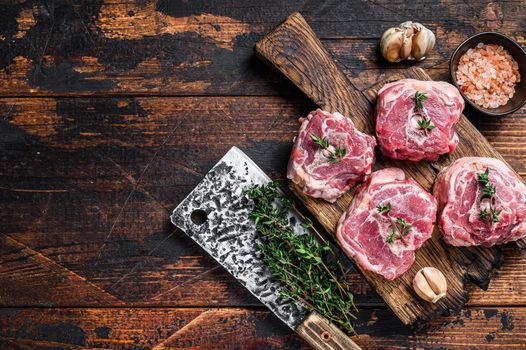 Raw mutton lamb neck meat on a butcher board with cleaver. Dark wooden background. Top view. Copy space.