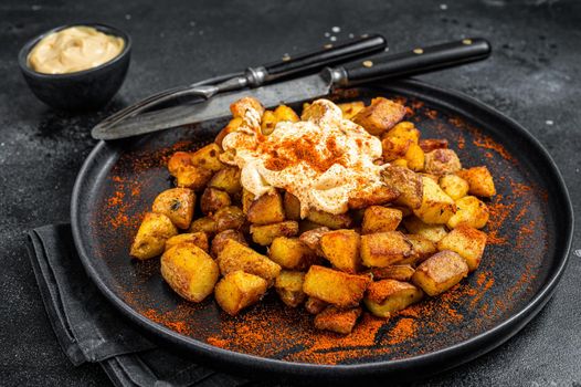 Patatas Bravas, traditional Spanish tapas, baked potato with spicy tomato sauce. Black background. Top view.