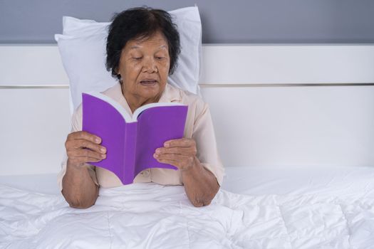 old woman reading a book on bed in bedroom