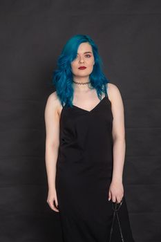 People and fashion concept - Woman dressed in black dress and blue hair posing over black background.