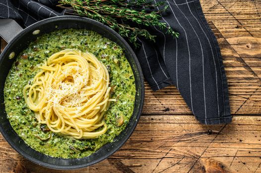 Pasta spaghetti with pesto sauce and fresh spinach and parmesan in a pan. Wooden background. Top view. Copy space.