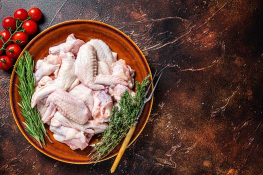 Cut Raw chicken wings in a rustic plate with thyme and rosemary. Dark background. Top view. Copy space.