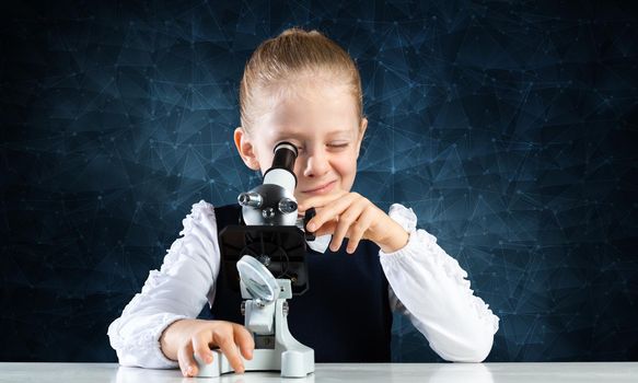 Little girl scientist looking through microscope in classroom at biology lesson. Research and discovery. Formal education in modern school. Schoolgirl in schoolwear making experiment in class.