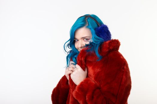 Animal protection, fashion and hair concept - beautiful girl wearing artificial fur coat with blue hair standing on white background.