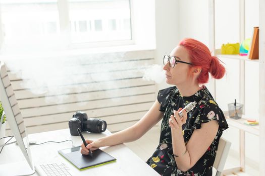 graphic designer concept - Female graphic designer working on computer while using graphic tablet at desk in the office and smoking a vape.