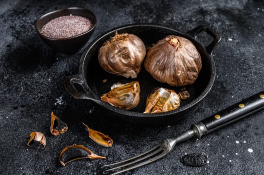 Bulbs of fermented black garlic in a pan. Black background. Top view.
