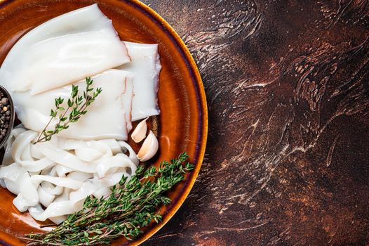 Sliced raw rings squid in a rustic plate with rosemary. Dark background. Top view. Copy space.