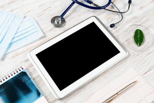 Medical diagnostics in modern hospital. Top view tablet computer with blank screen, x-ray image, stethoscope and cardiogram on wooden desk. Professional healthcare and digital technology in clinic.