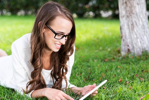 portrait of young woman with digital tablet laying on grass