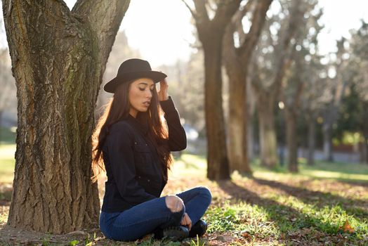 Portrait of thoughtful woman sitting alone outdoors wearing hat. Nice backlit with sunlight