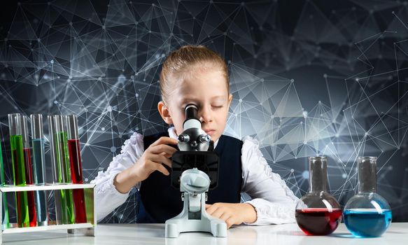 Little girl scientist looking through microscope in classroom at chemistry lesson. School chemical laboratory with glass flasks and test tubes. Schoolgirl making experiment in chemistry class.