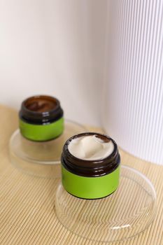 Focus on opened jar of facial cosmetic cream with green space for brand, on white cube. Concept of cluelty free, organic, kosher cream is great for dry and rough skin.
