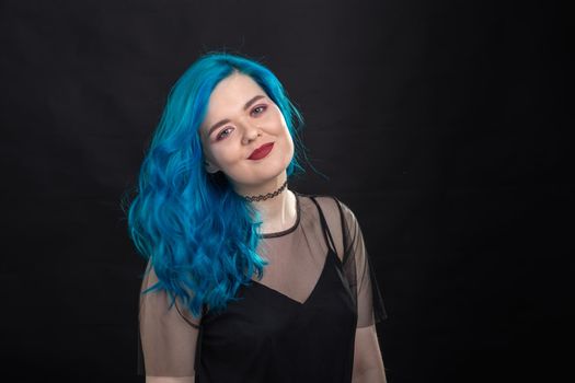 Style, fashion and hair concept - close-up portrait of young woman in black dress with blue hair on black background.