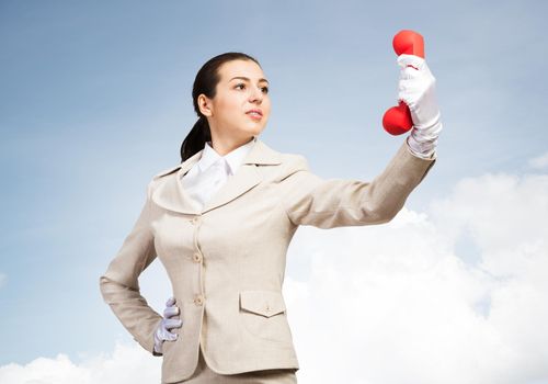 Beautiful woman holds red handset phone on distance. Operator in business suit posing with cellphone on blue sky background. Business assistance and consultation. Customer service support concept