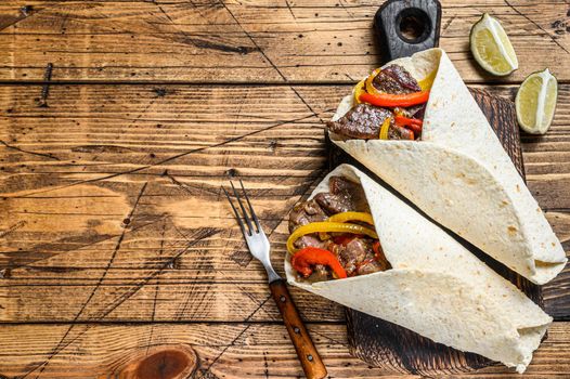 Fajitas Tortilla wrap with beef meat stripes, colored bell pepper and onions and salsa. Wooden background. Top view. Copy space.