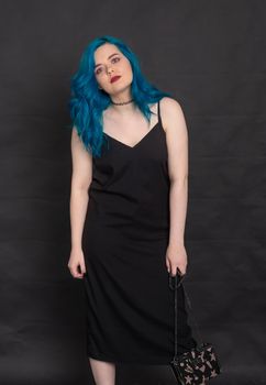 People and fashion concept - Woman dressed in black dress and blue hair posing over black background.