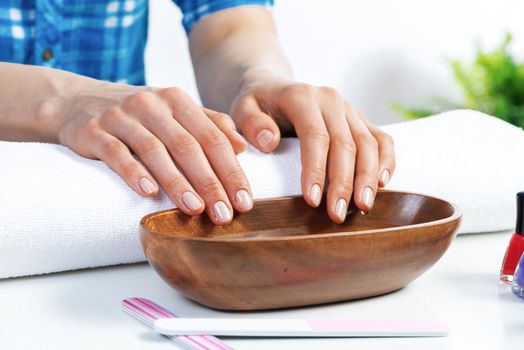 Closeup female hands in wooden bowl with water. Spa procedure and relaxation. Female hands preparing for manicure. Professional nail care and beautician service. Beauty and hygiene concept