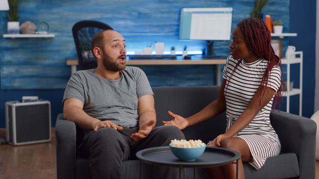 Married interracial people with marriage problems yelling at each other in living room. Mixed race young couple fighting at home while sitting on sofa, having argument and being irritated