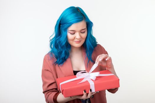 People, holidays and fashion concept - Surprising woman with blue hair holding a gift box on white background.