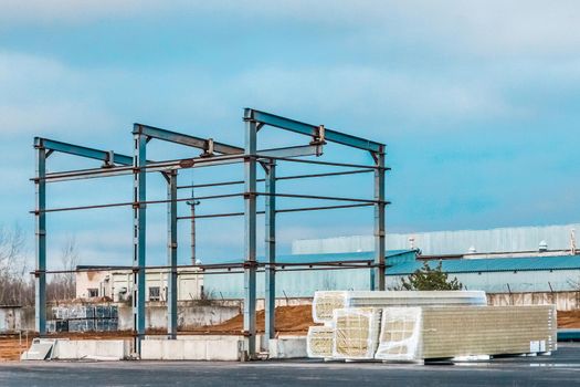 Metal frame of a new modern building under construction and packed sandwich panels at a construction site.