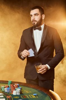 A young man in a business suit standing near poker table. Man gambles. The player at the gaming table playing cards.