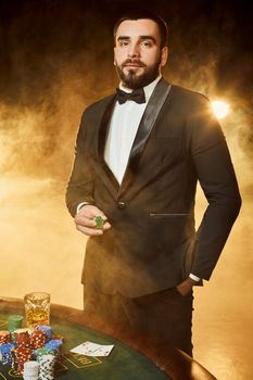 A young man in a business suit standing near poker table. Man gambles. The player at the gaming table playing cards.