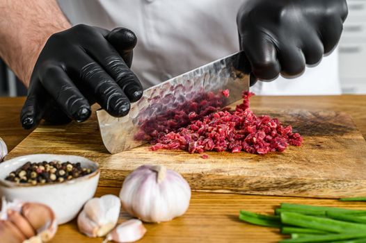 Man cutting raw beef meat. A chef in black gloves. Concept of cooking beef tartare.