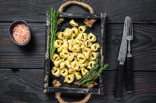 Italian traditional tortellini pasta with spinach in a wooden tray. Black wooden background. Top view.