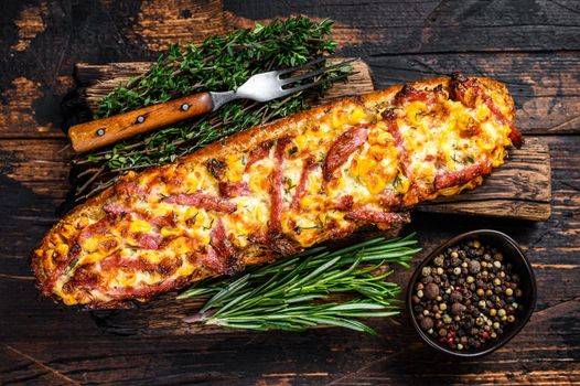 Baguette stuffed with ham, bacon, vegetables and cheese on wooden board. Dark wooden background. Top view.