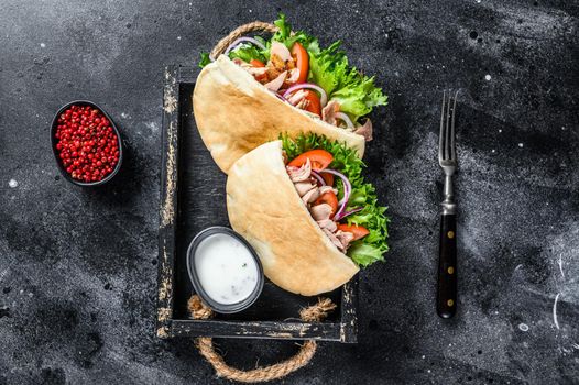 Doner kebab with grilled chicken meat and vegetables in pita bread on a wooden tray. Black background. Top view.