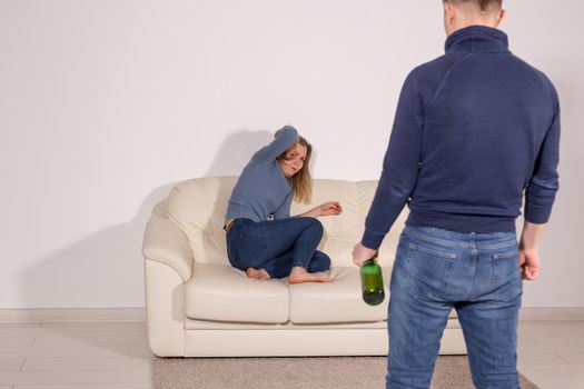 People, violence, alcoholism and abuse concept - Man with bottle alcohol while wife is lying on sofa.