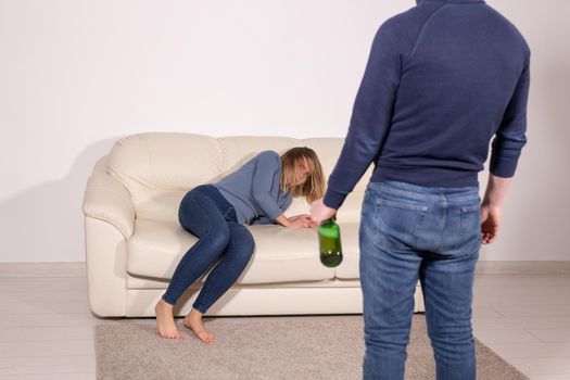 People, violence and abuse concept - Man drinking alcohol while wife is lying on sofa.