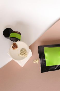 Black doy pack and jar with cosmetic products and green space for your brand, clay powder on white plate. Concept of facial mask ingredients and homemade organic cluelty free, kosher cosmetic for skin and pampering.