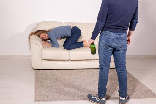 People, violence and abuse concept - Man drinking alcohol while wife is lying on sofa.