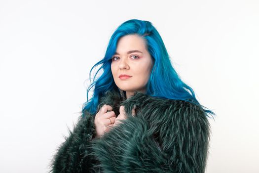 Animal protection, fashion and people concept - beautiful girl dressed in artificial fur coat with blue hair standing on white background.