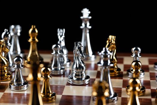 Gold and silver chess figures standing on chessboard. Intellectual and tactic game. Strategy planning, leadership and teamwork business concept. Close-up metal chess pieces on black background.