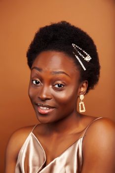 young pretty african model with golden jewelry in fashion style dress smiling happy on brown backround, lifestyle people concept close up